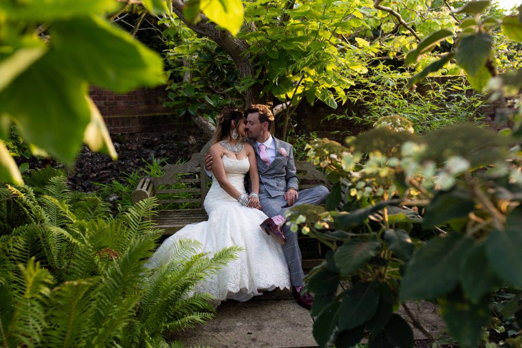 bride and groom sitting on bench surrounded by foilage and plants