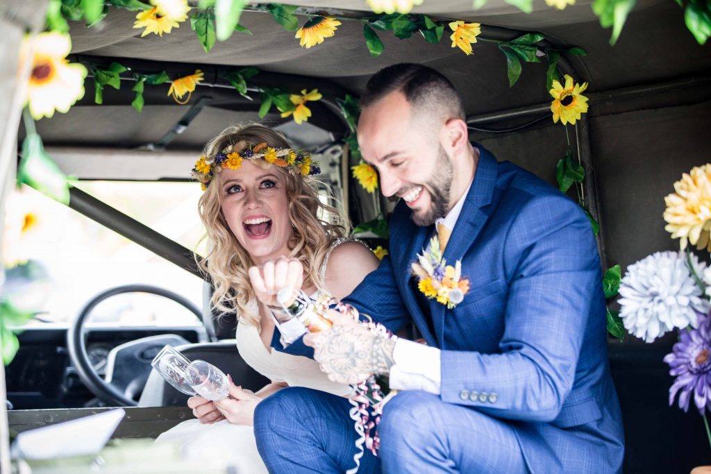bride and groom smiling with champagne in Land rover car