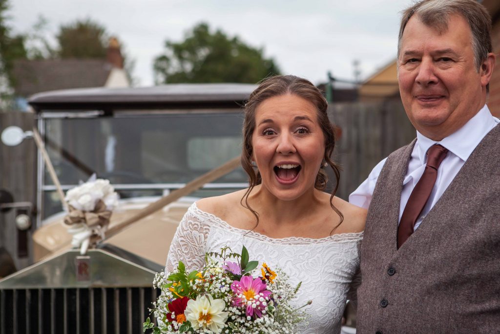 bride with father posing by vintage wedding car