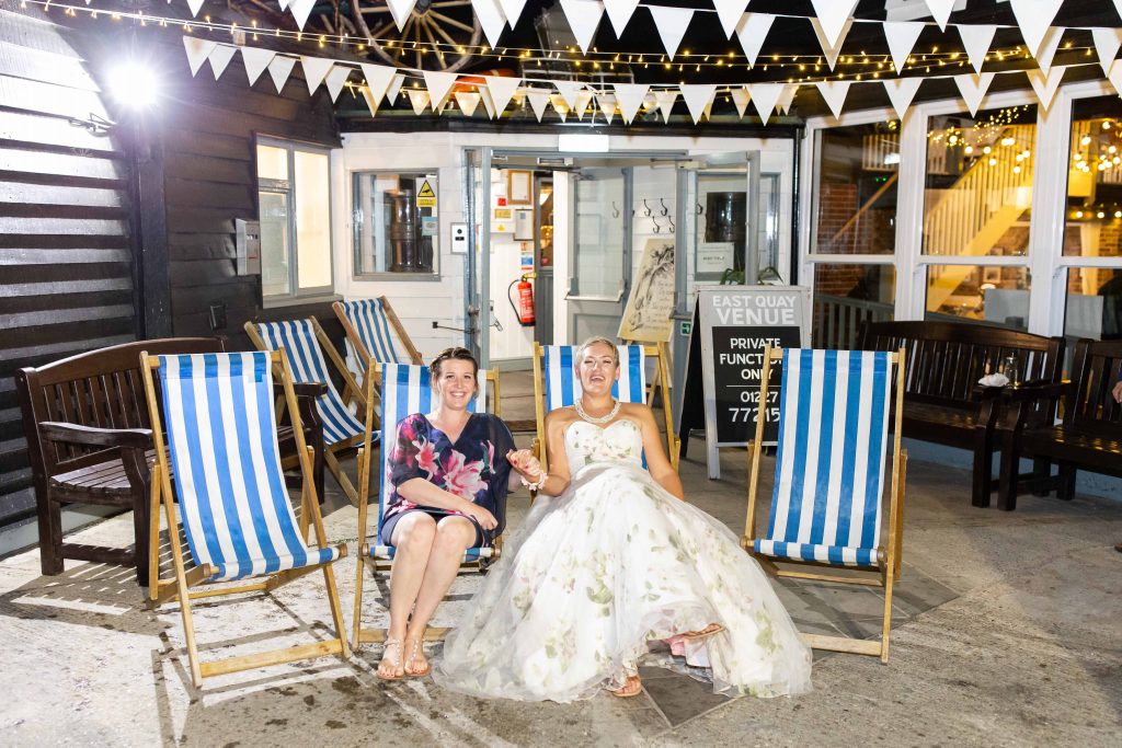 bride with best friend on deckchairs outside East Quay wedding venue