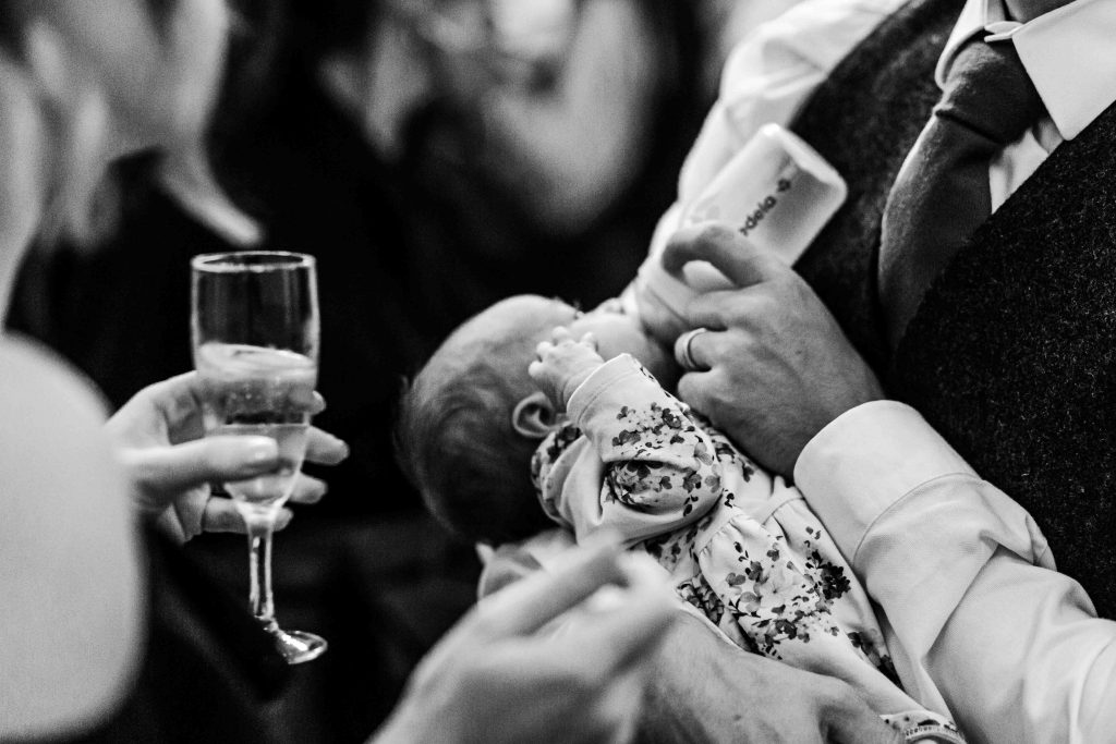 baby drinking milk at wedding while guest drinks champagne
