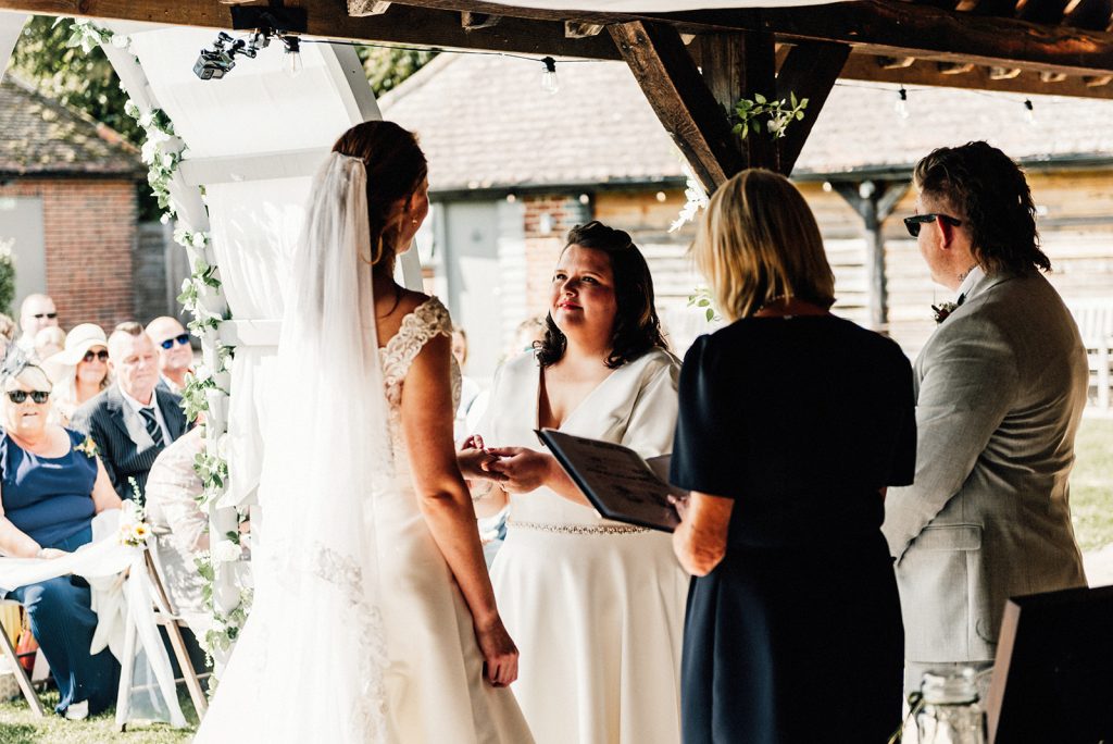 2 brides exchanging rings in outdoor wedding ceremony at The Night Yard wedding venue