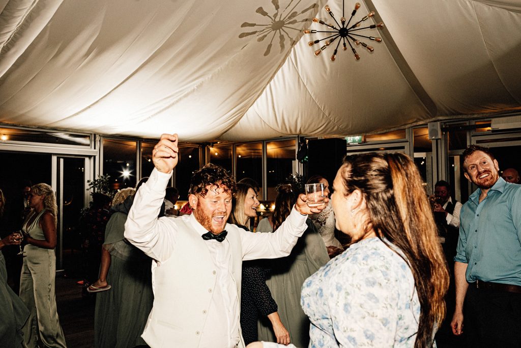 dance floor action at wedding with wedding guest smiling dancing with hands in air