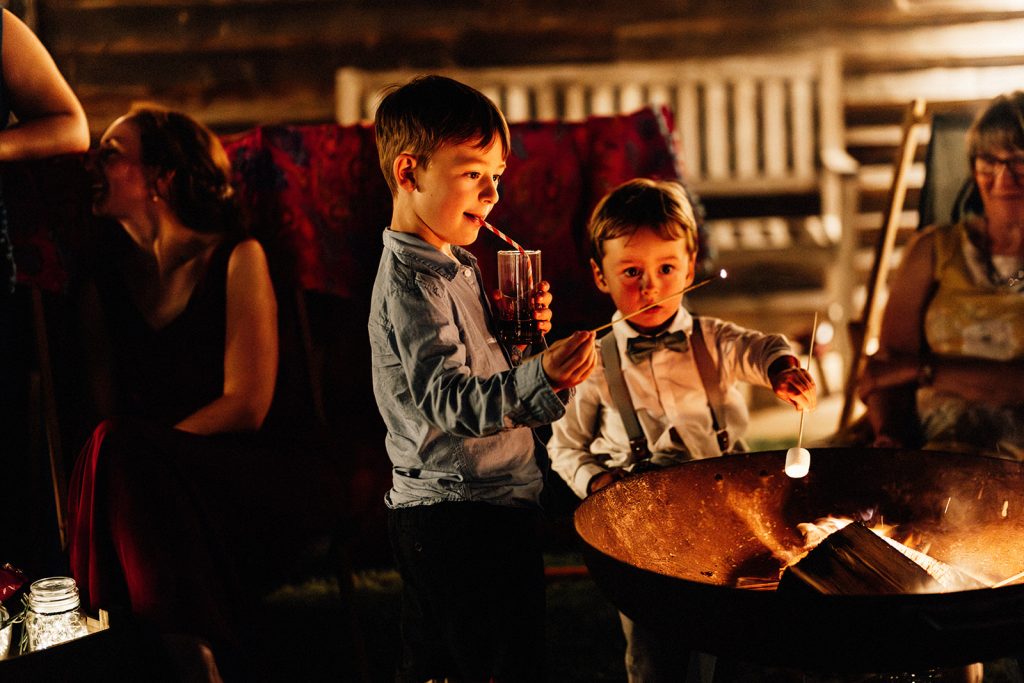 2 boys toasting marshmallows over a firepit at night at The Night Yard wedding venue