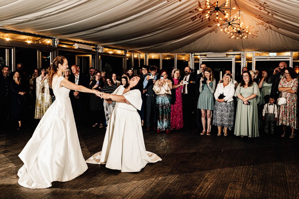 a first dance at The Night Yard wedding venue with 2 brides surrounded by their guests.