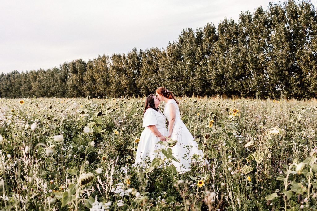 wedding portrait with 2 brides kissing in a field of sunflowers