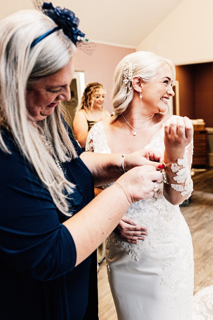 mother of bride helping with fasteners on brides dress sleeve