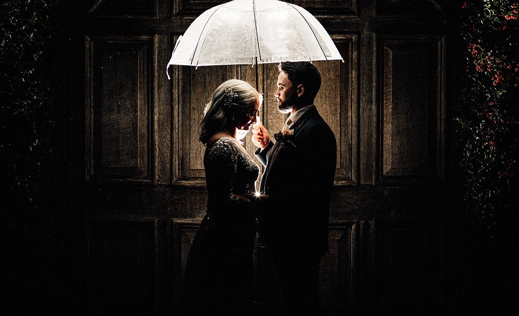 flash portrait of bride and groom at night under an umbrella in front of the doors at winters barns wedding venue.