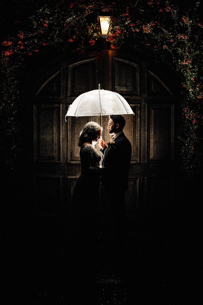 flash portrait of bride and groom at night under an umbrella in front of the doors at winters barns wedding venue.