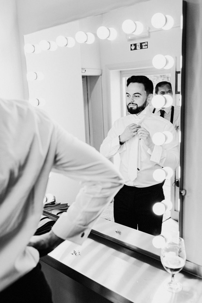 groom adjusting his tie in mirror during groom prep