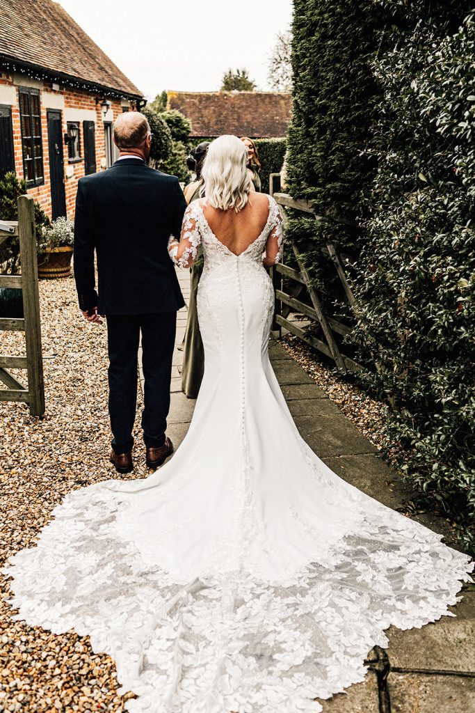 bride's dress captured from behind holding on to her fathers hand while waiting to walk down the aisle