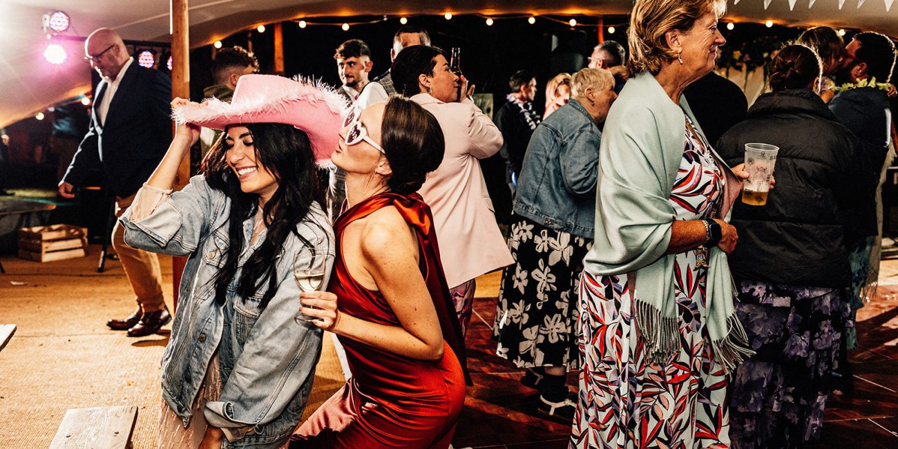 wedding guests in tipi on dancefloor dancing and posing with pink cowboy hat and heart shaped sunglasses on