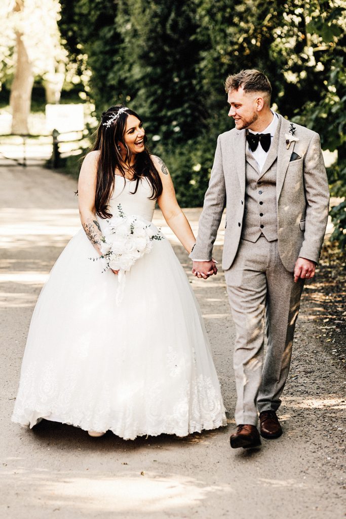 wedding portrait of bride and groom walking and smiling towards camera captured by Chiham Village Hall wedding photographer