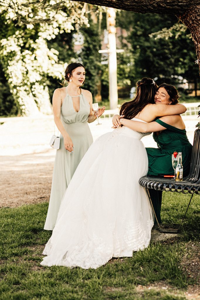 bride hugging a bridesmaid with guest looking on