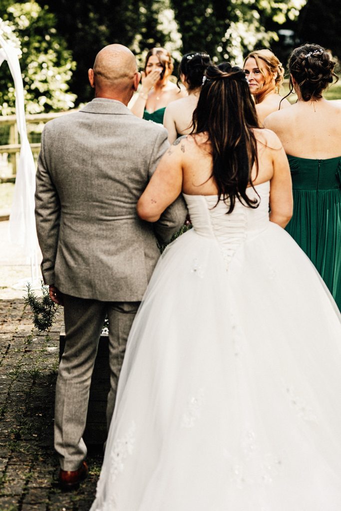 bride linking arms with her dad photographed from behind with her bridesmaids