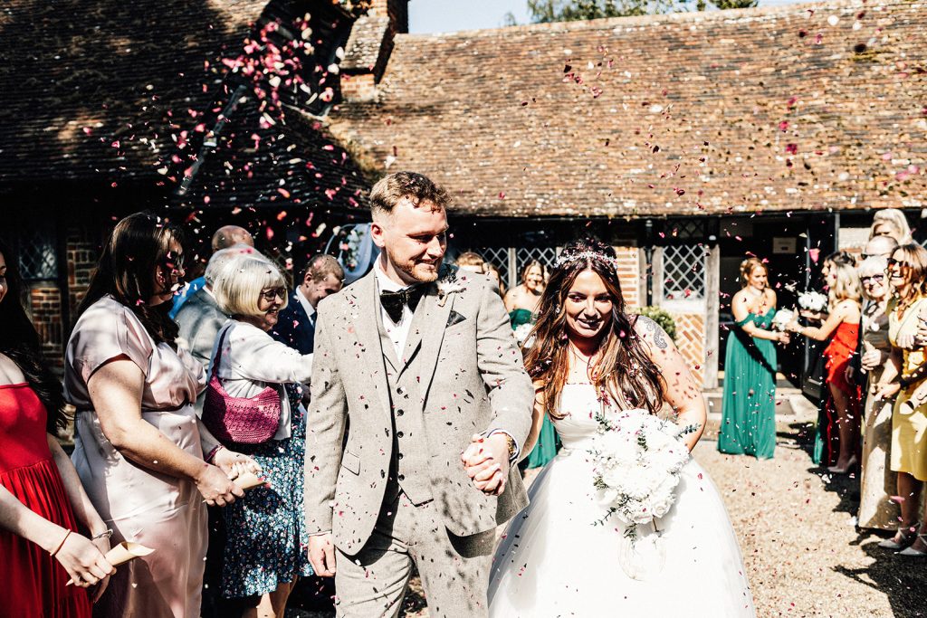 A bride and groom making their exit amidst a shower of confetti outdoors.