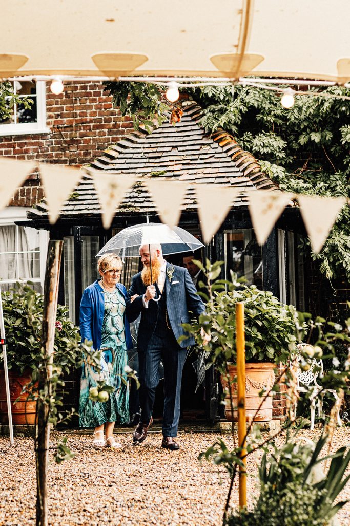 Groom and his mum walking in rain with umbrella at a Guston Court Wedding