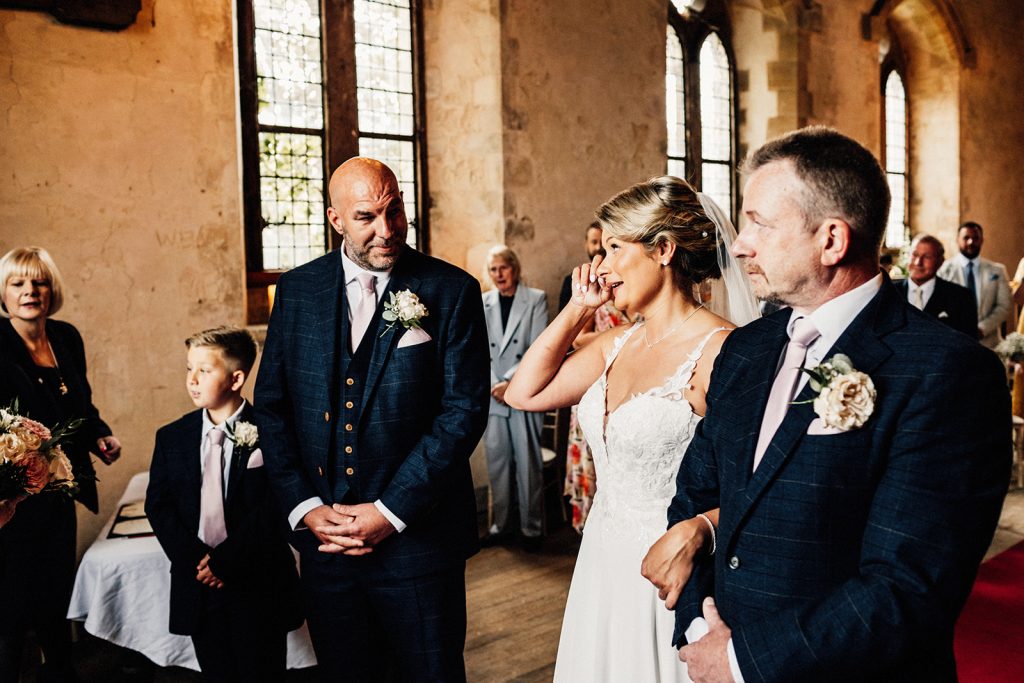 Bride wiping away tear at seeing groom at wedding ceremony