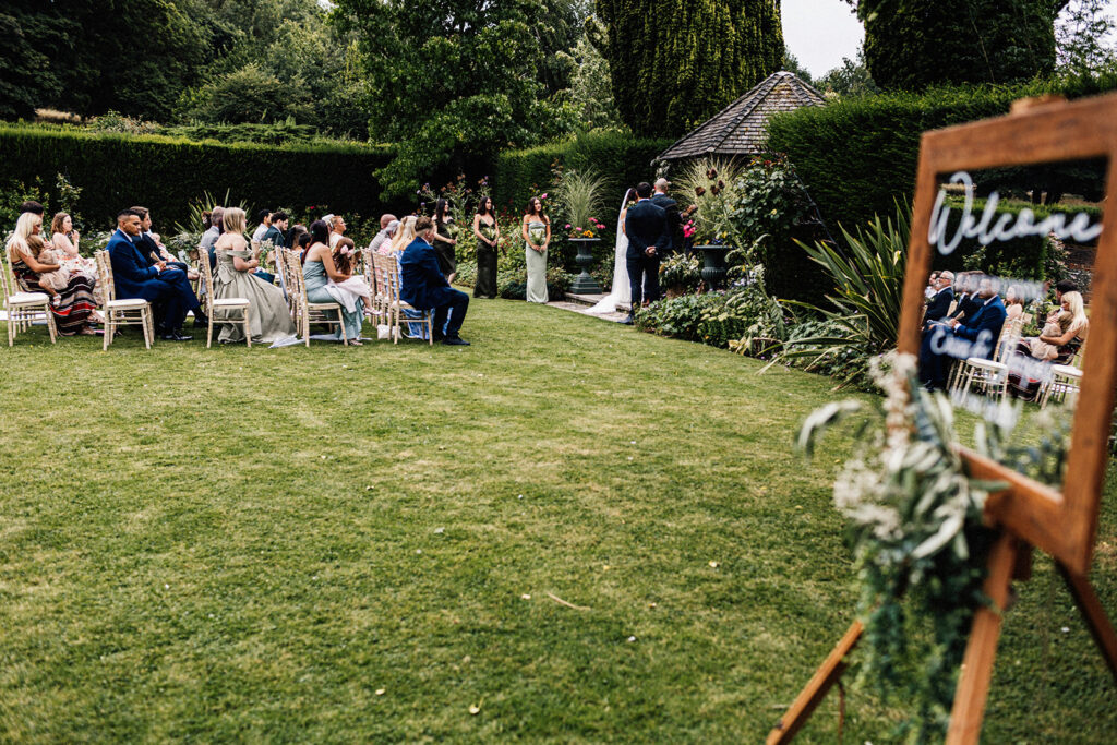 outdoor wedding ceremony showing seated guests on the lawn looking at bride and groom at Swarling Manor wedding venue.