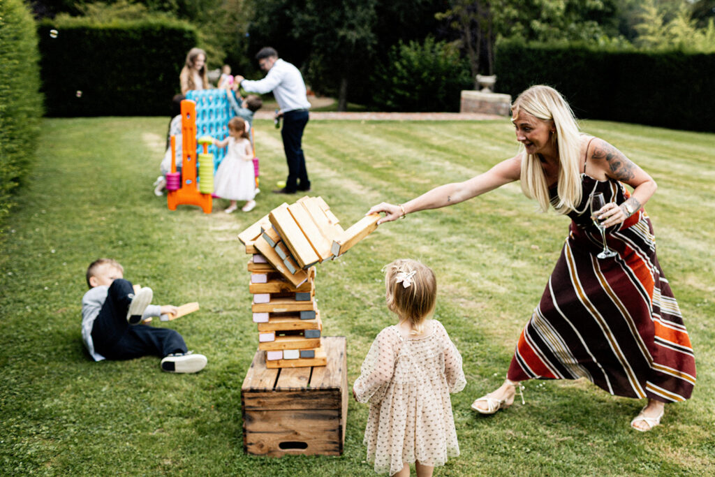 mum at a Swarling manor wedding playing a large wooden jenga game with her young kids as it comes tumbling down on her go.