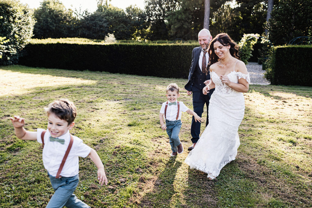 bride and groom with their two young boys running towards the camera laughing in the gardens of Swarling Manor wedding venue.