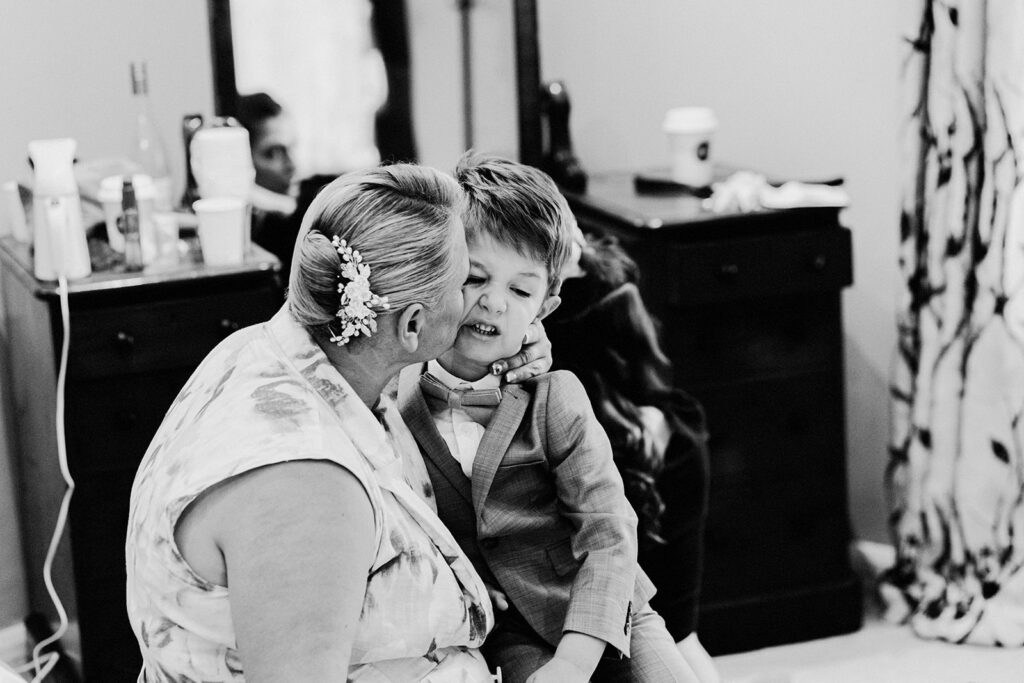 grandma hugging her young grandson in his wedding suit who is sat on her knee close and kissing him at a Swarling Manor wedding.