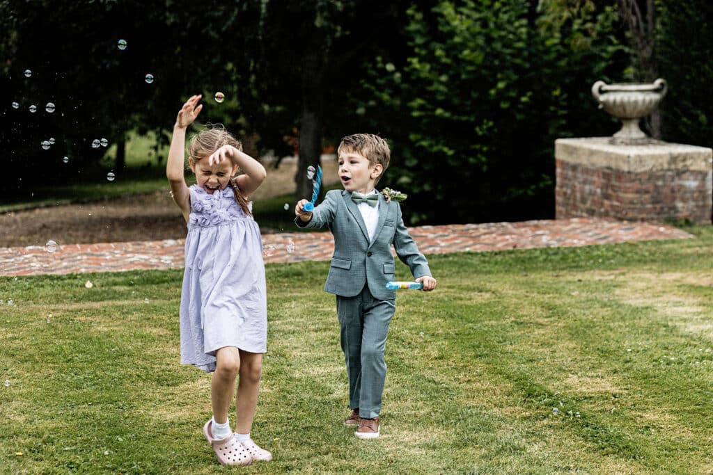 young boy with a bubble wand waving bubbles all around a young girl who is trying to escape them at a Swarling Manor wedding.