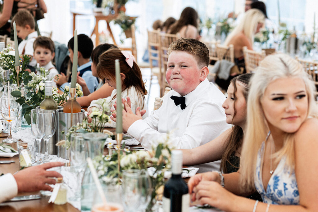 boy smiling at camera while seated at a table with other children at a Swarling manor wedding breakfast.