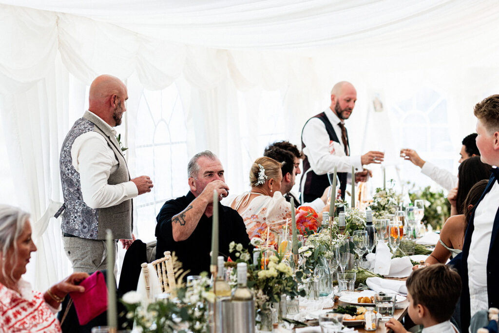 wedding guests at wedding breakfast clinking and toasting shot glasses in the marquee of Swarling manor wedding venue.